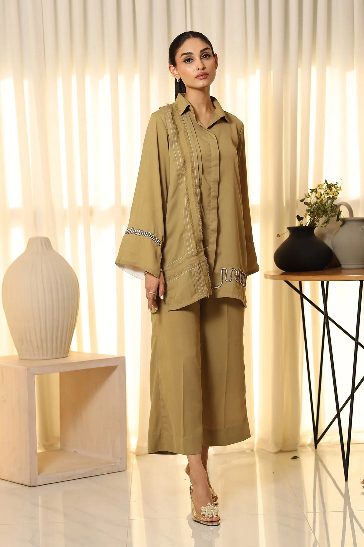 Woman in a beige outfit standing in a room with decorative elements.
