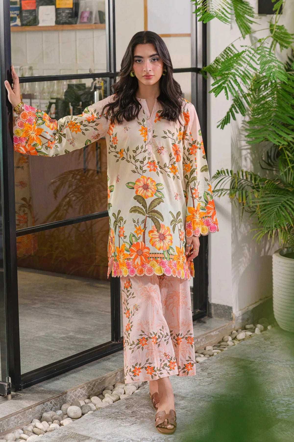 Model in a full-length pose wearing a light pink floral printed kurta set with embroidered scalloped borders and wide-leg trousers.
