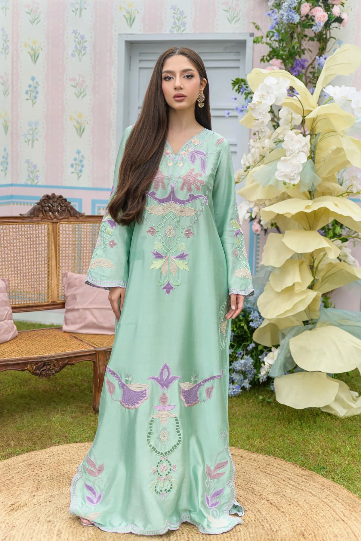 Woman in a light green embroidered dress standing in a decorated outdoor setting with flowers and a bench.


