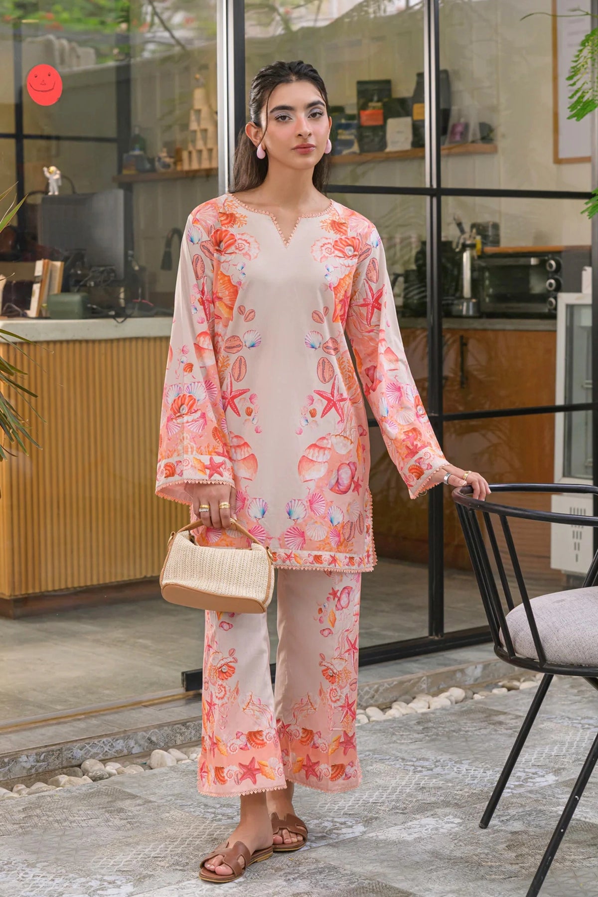 Model wearing a light pink co-ord set with orange seashell and starfish prints, paired with straight trousers.
